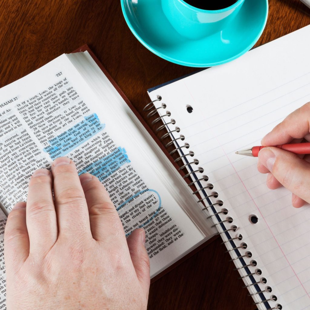 Person with Bible open on left side and notebook open on right side