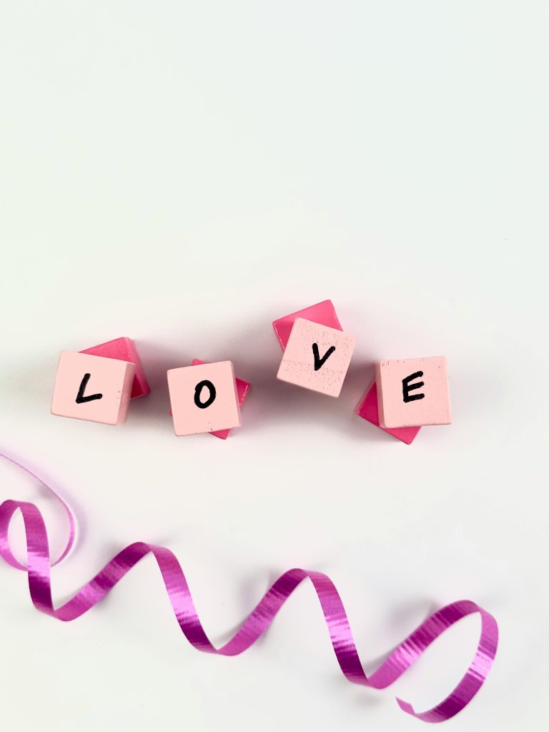 Pink blocks spelling 'LOVE' with a playful pink ribbon on a white background.